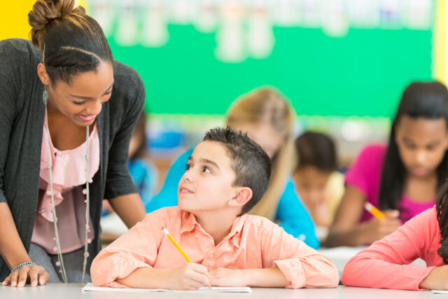 photo - Teacher Helping Student at Desk in Classroom