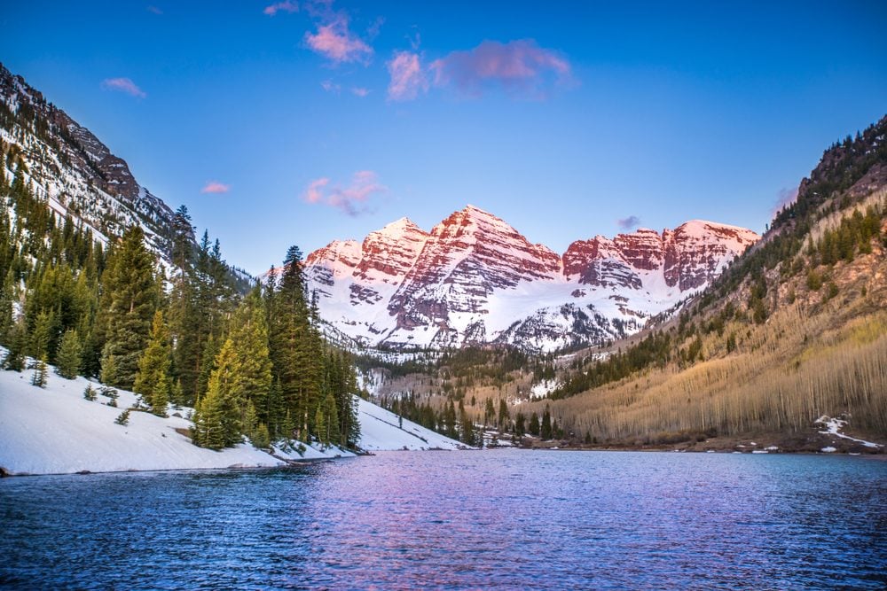 The Rocky Mountains near Aspen, Colorado glow in the light of the morning sunrise, as the mountains and trees reflect off the lake.