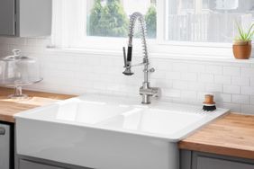 A kitchen sink detail with a butcher block wood countertop, white subway tile backsplash, grey cabinets, and a farmhouse sink.