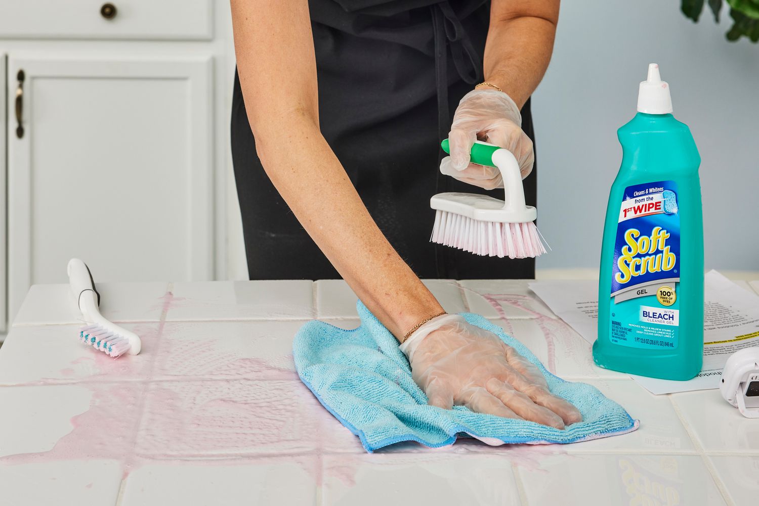 A person uses a microfiber and Soft Scrub Gel Cleanser with Bleach to clean a white tile countertop