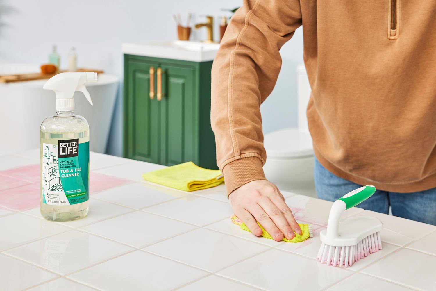 A person cleans a white tile countertop using Better Life Natural Tub and Tile Cleaner