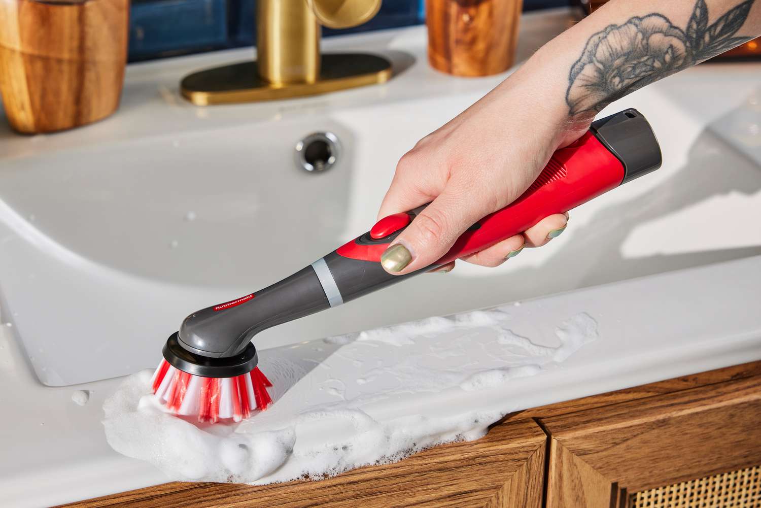 Hand holding the Rubbermaid Reveal Power Scrubber to clean a soapy bathroom sink