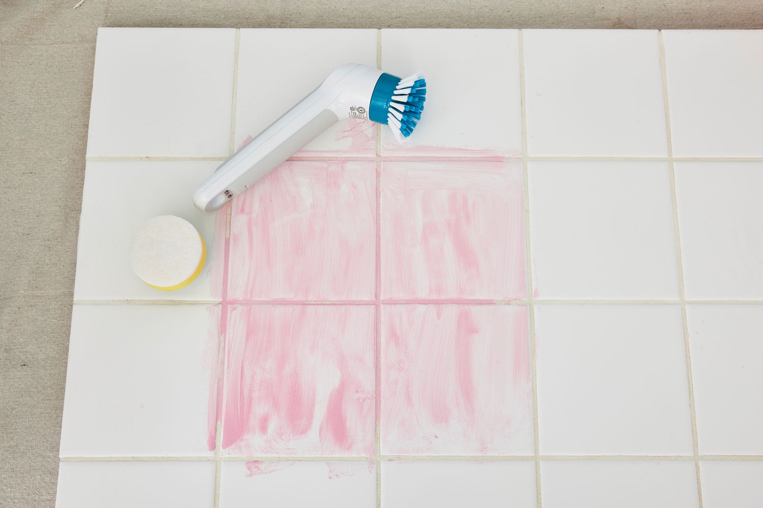 A Black+Decker Grimebuster Pro Power Scrubber Brush lying on white tile marked with red