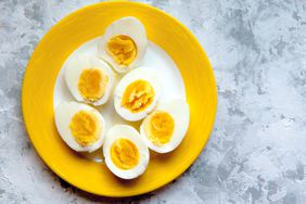 overhead view of hard boiled egg halves on a yellow plate and grey surface