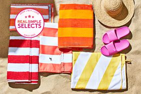 Folded beach towels we recommend displayed on sand next to beach shoes and a straw hat 