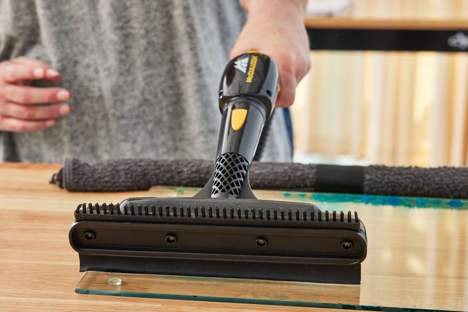 A person uses the McCulloch MC1385 Deluxe Canister Steam Cleaner to clean glass