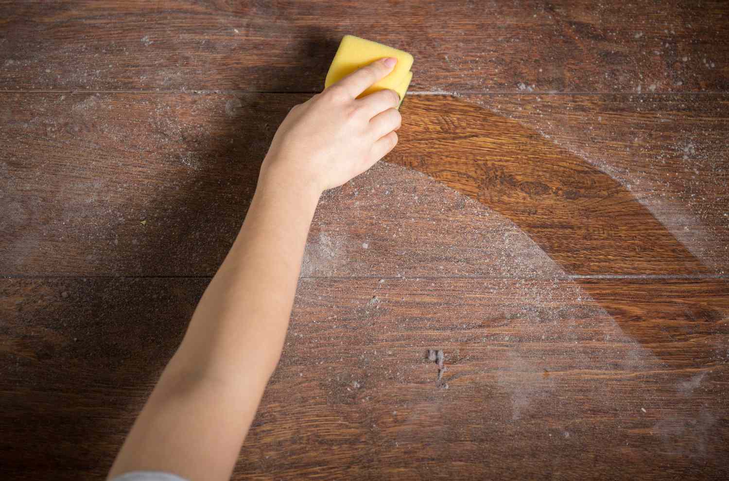 Close up of yellow sponge cleaning dust from a wood table