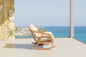 A single patio rocking chair with beige canvas cushions with a water view