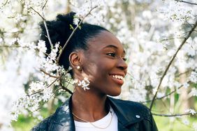 Beautiful young black girl smiling against blossom spring trees.