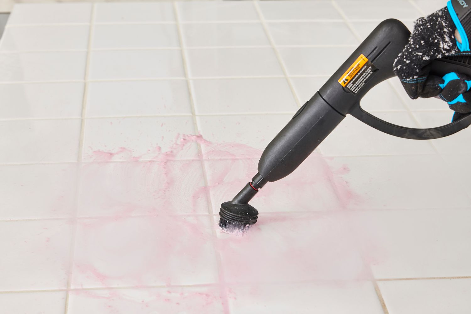 Hand holds a Wagner 915e On-Demand Power Steamer while cleaning white tile