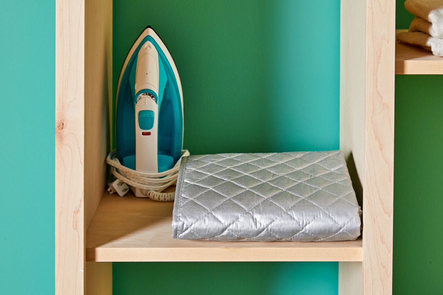 The BNYD Portable Ironing Mat Blanket folded on a shelf next to an iron