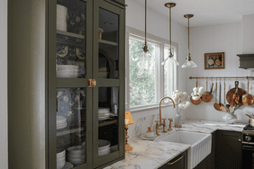 Sage green kitchen cabinets, flower wallpaper inside, brass kitchen faucet and farmhouse sink