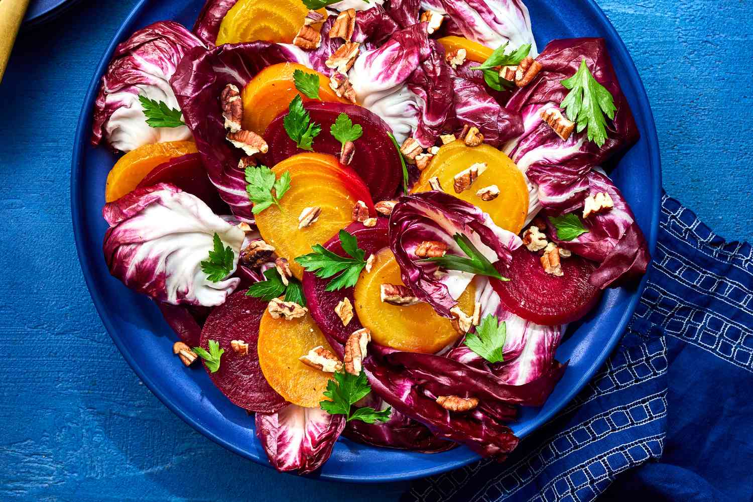 overhead view of greens and yellow beet salad on blue background