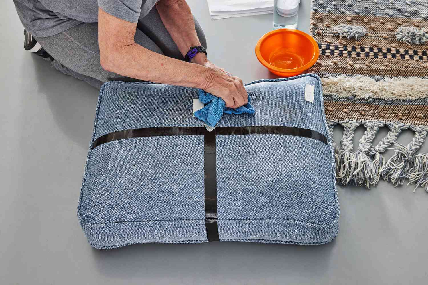 A person scrubbing stains off a cushion using Bissell Advanced Oxy Stain Pretreat and a rag.