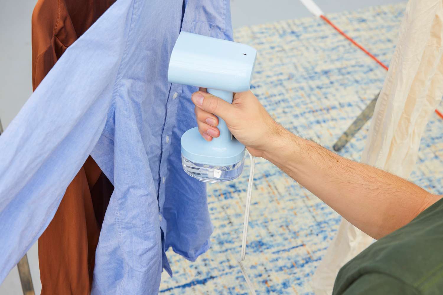 A person using the Proctor Silex Compact 2-in-1 Garment Steamer/Iron to steam a shirt.