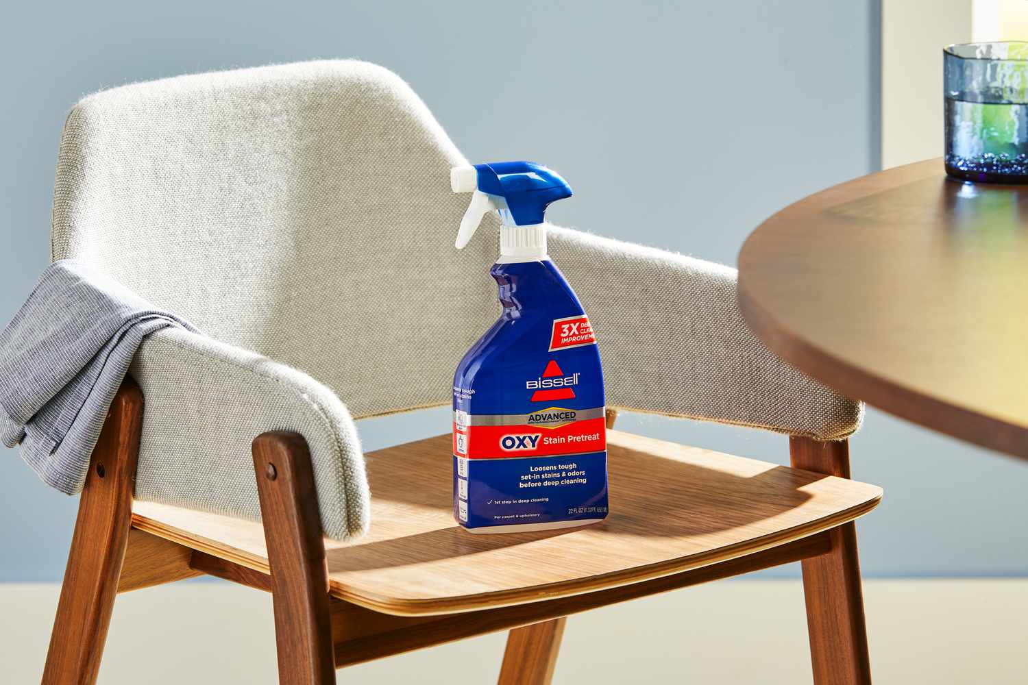 A bottle of Bissell Advanced Oxy Stain Pretreat sitting on a modern dining chair.