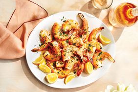 Grilled Shrimp With Lemon Wedges on a White Serving Platter Against a Pale Pink Tablecloth
