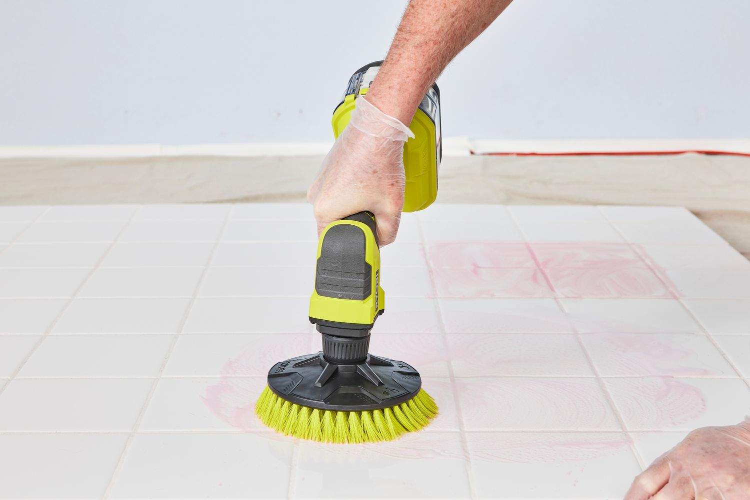 Person cleans white tile with a Ryobi One+ 18V Cordless Compact Power Scrubber