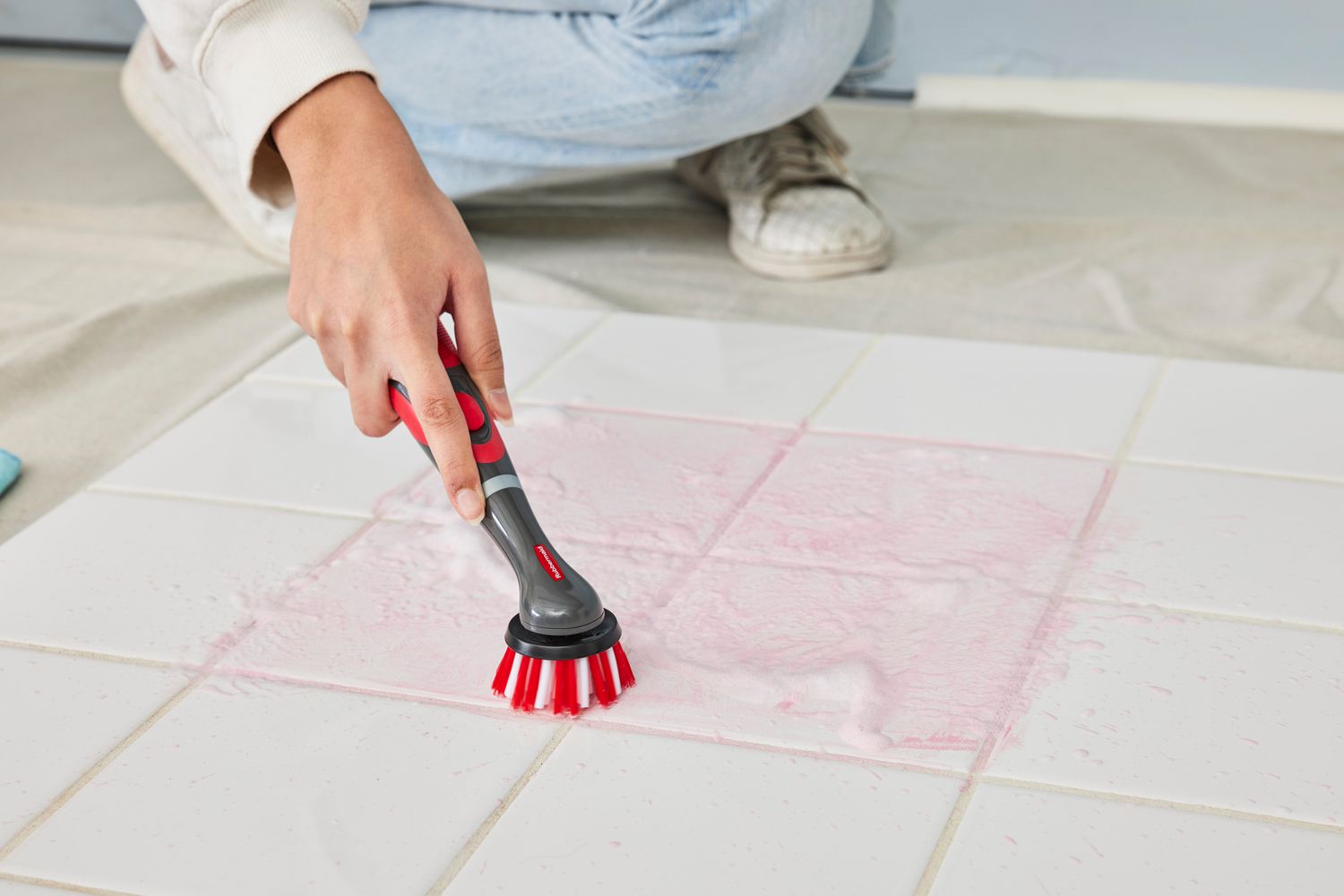 Person cleans white tile stained with red marker with a Rubbermaid Reveal Cordless Battery Powered Scrubber Home Kit