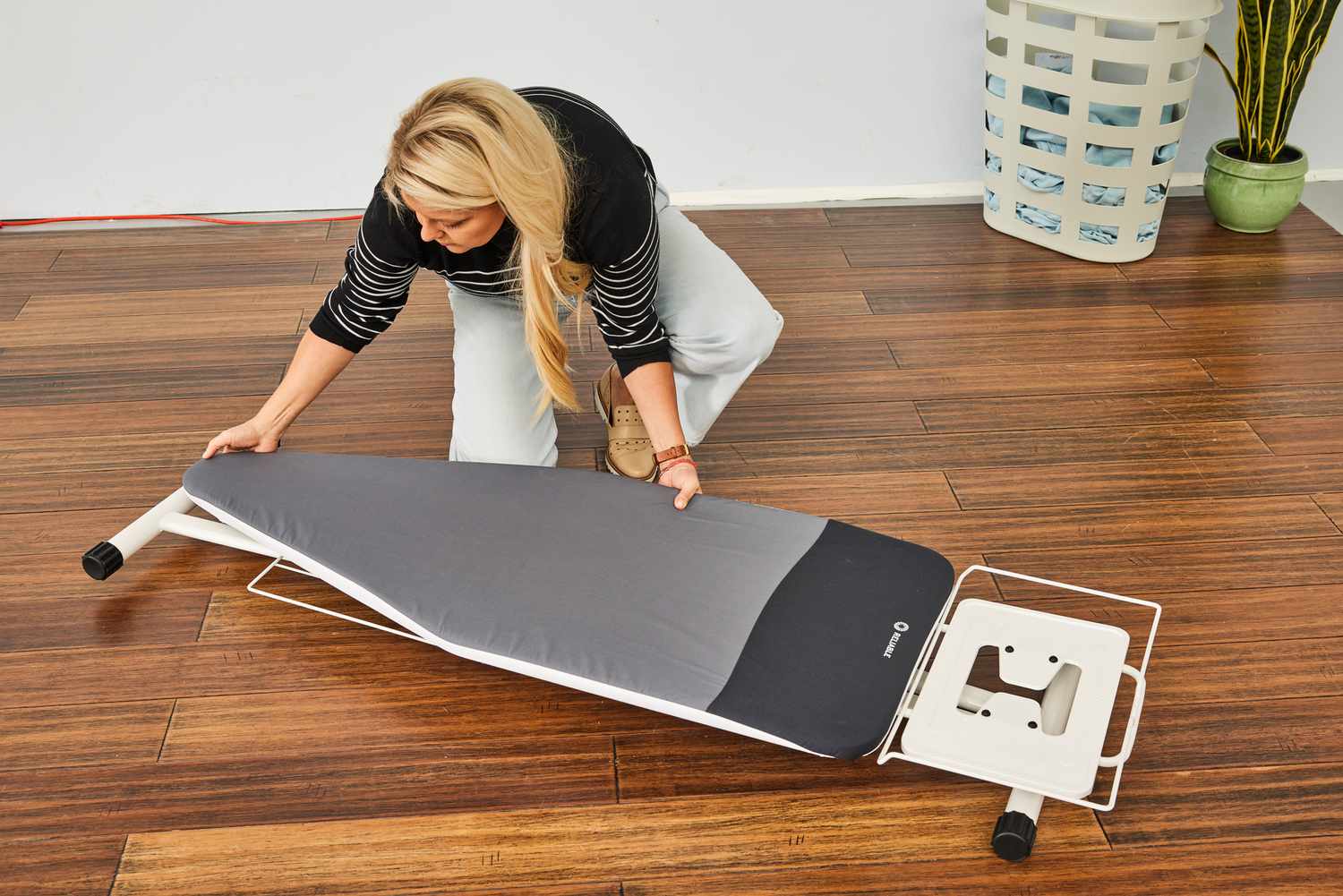 A person laying the Reliable 320LB Home Ironing Board onto a wooden floor