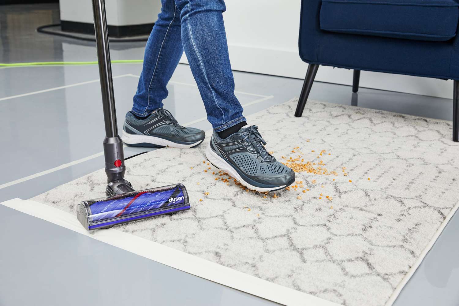 Dyson V12 Detect Slim beside a foot stepping on food on a rug