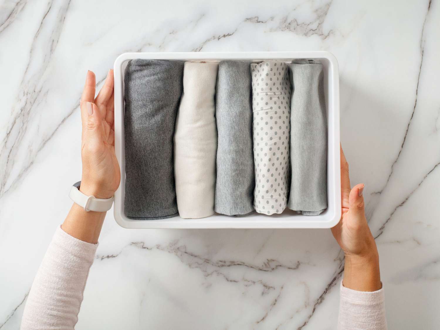 Woman hands neatly folding underwears and sorting in drawer organizers on white marble background