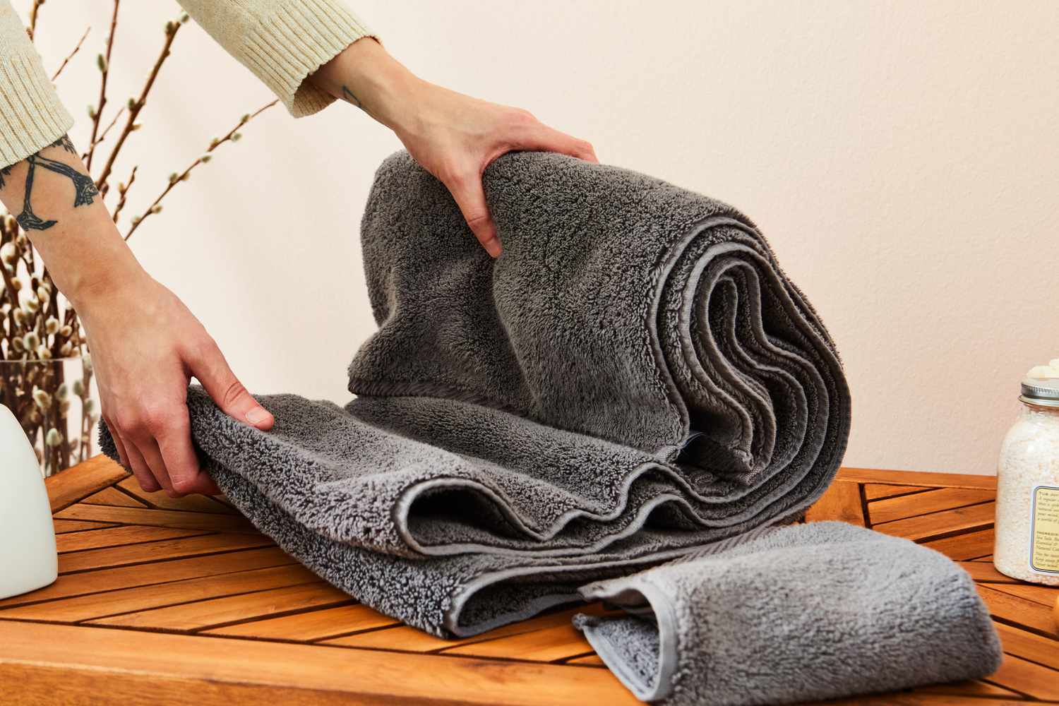 Person folding Matouk Milagro Cotton Bath Towel on wood table