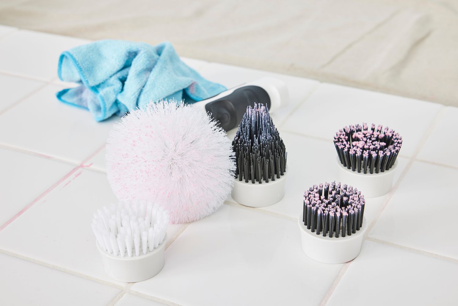 Various brush attachments for the Klever Electric Spin Scrubber with 8 Brushes sitting on white tile