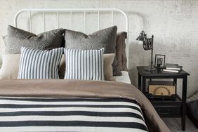 White Frame Bed With Black and White Striped Duvet Cover and Cushions, Next to a Black Side Table and Lamp