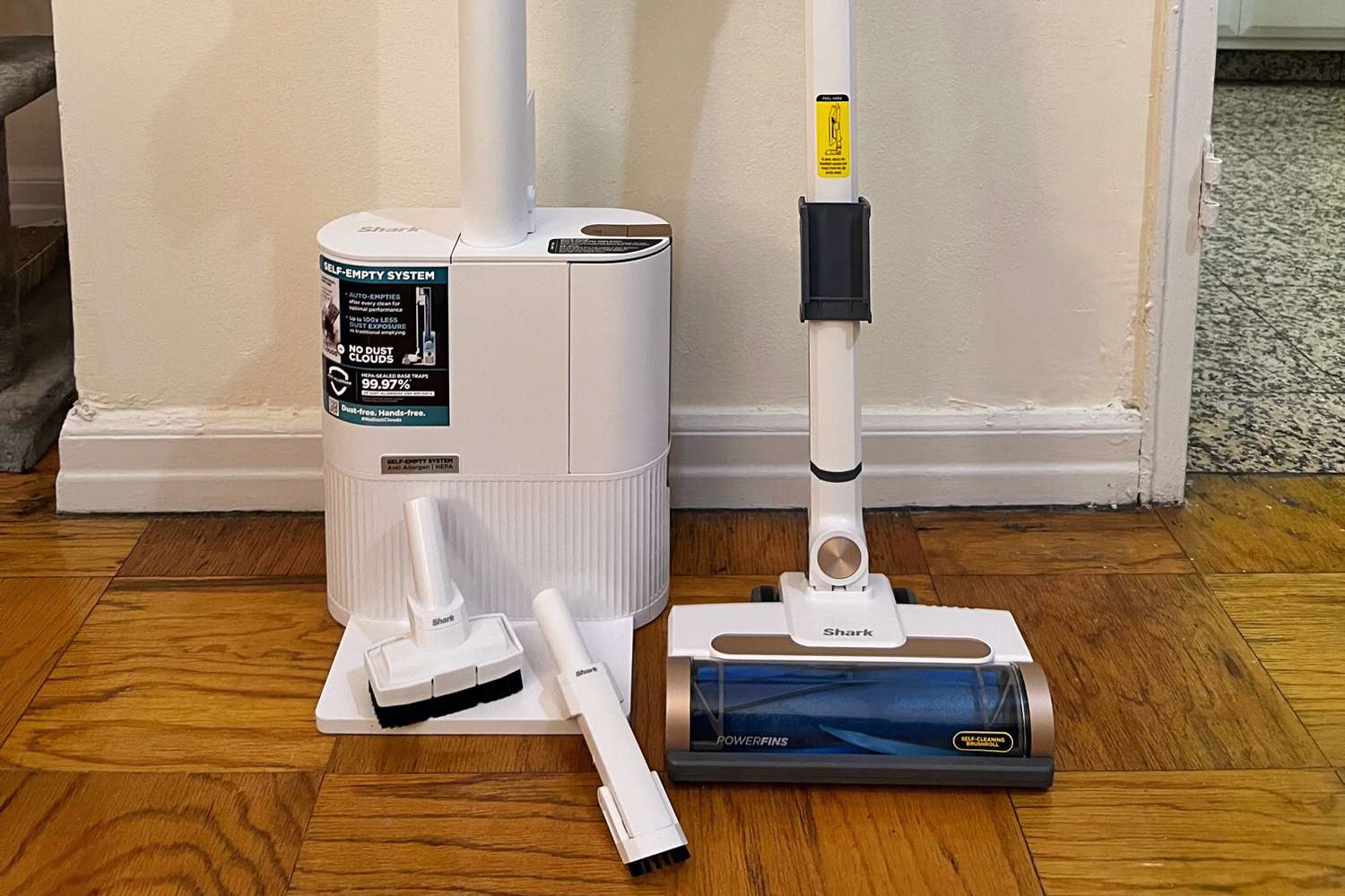 Shark Wandvac Cordless Stick Vacuum with Self-Empty Charging Base and attachments on a wood floor.