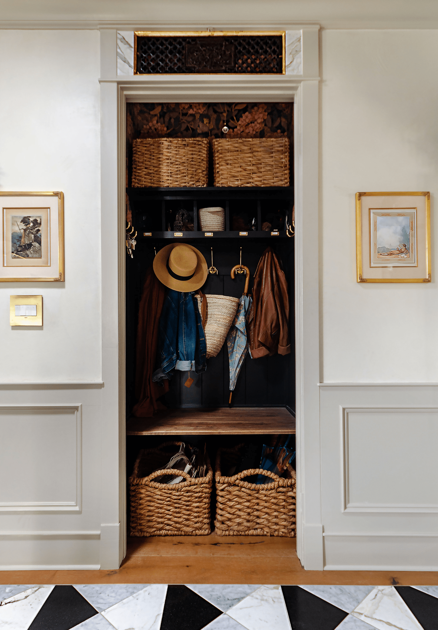 Closet with dark paint and moody wallpaper, brass hooks and woven baskets