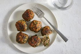 top view of six Spinach and Lamb Meatballs, one cut in half on white plate with a metal fork