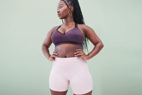 Studio shot of a young woman wearing gym gear with her hands on her hips against a green background