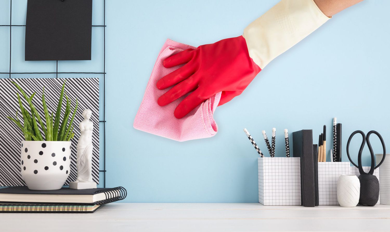 A person cleans a painted wall with a pink cloth while wearing a red cleaning glove