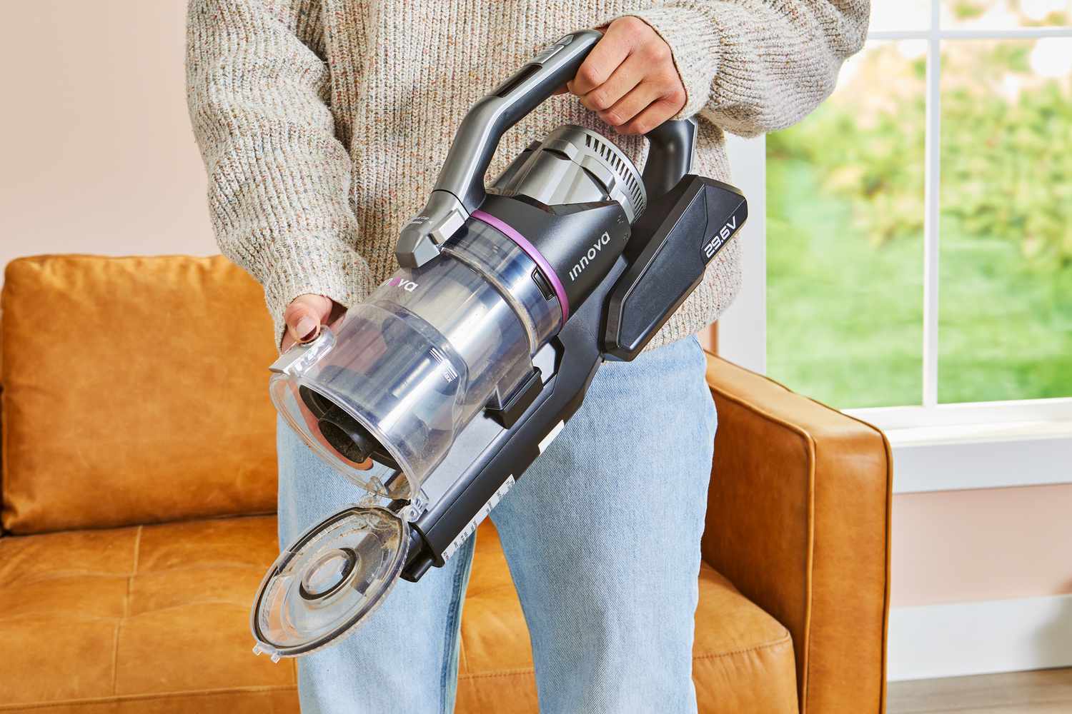 Person holding up an opened Innova Cordless Stick Multi-Surface Vacuum in a living room 