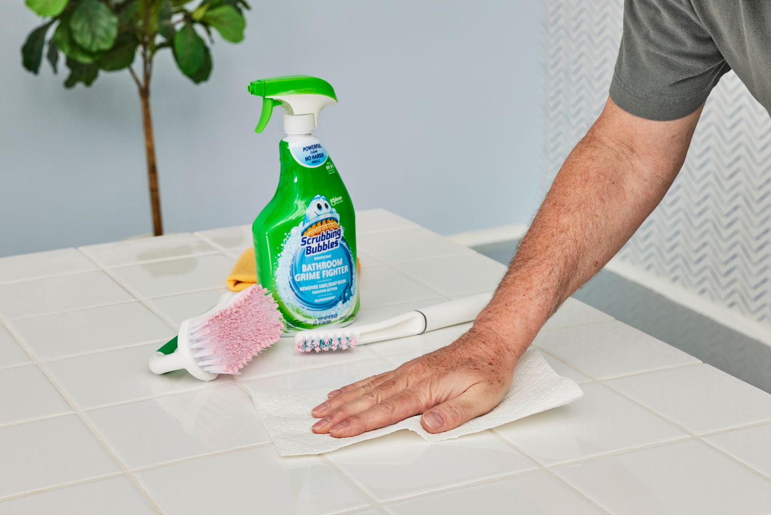 A person uses Scrubbing Bubbles Disinfectant Bathroom Grime Fighter Spray to clean a white tile countertop