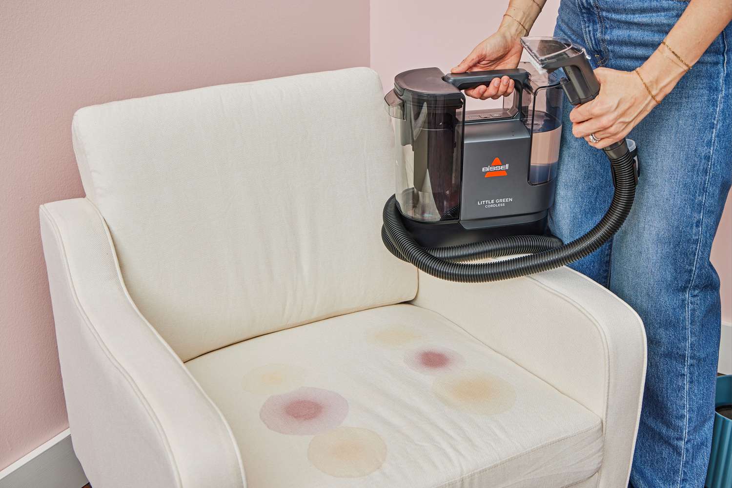 A person uses the Bissell Little Green Cordless Portable Carpet Cleaner 3682 to clean a stained white chair