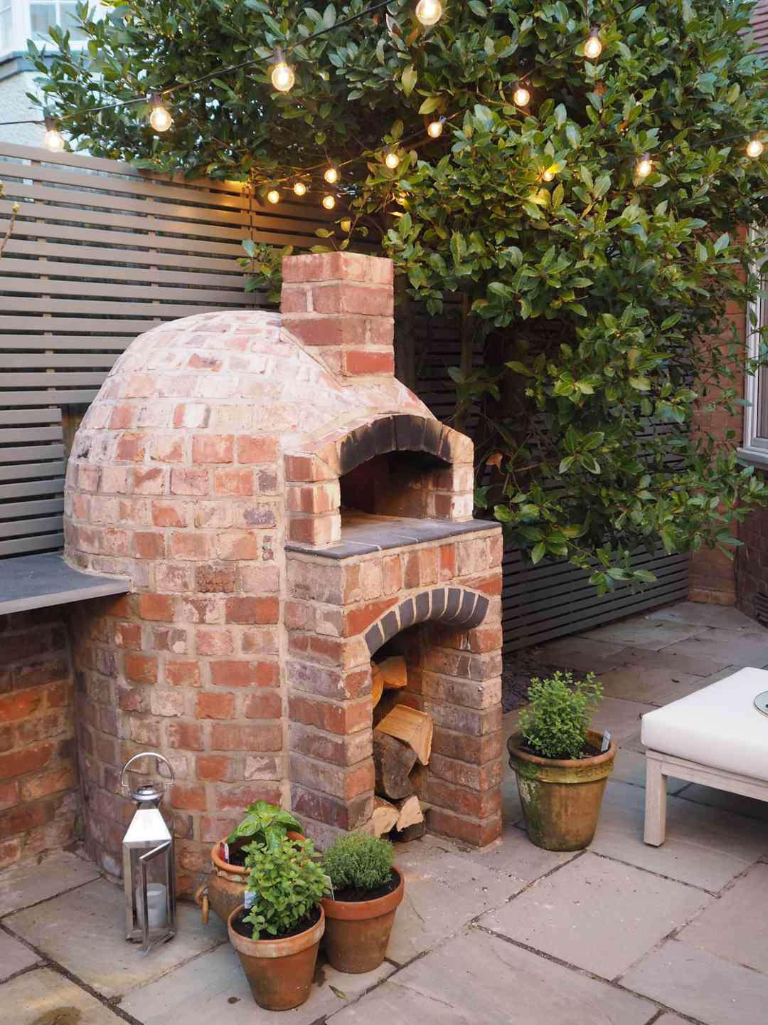 brick pizza oven in small patio area with string lights