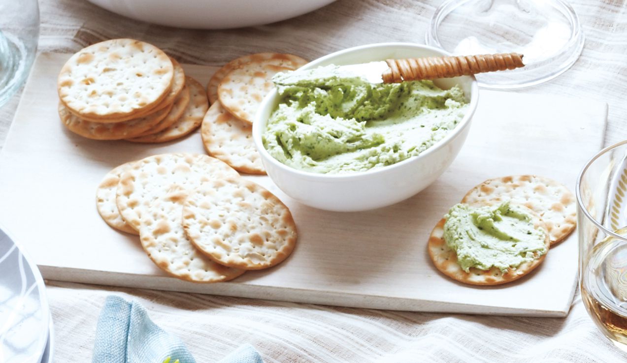 Goat cheese spread is served in a bowl alongside crackers.