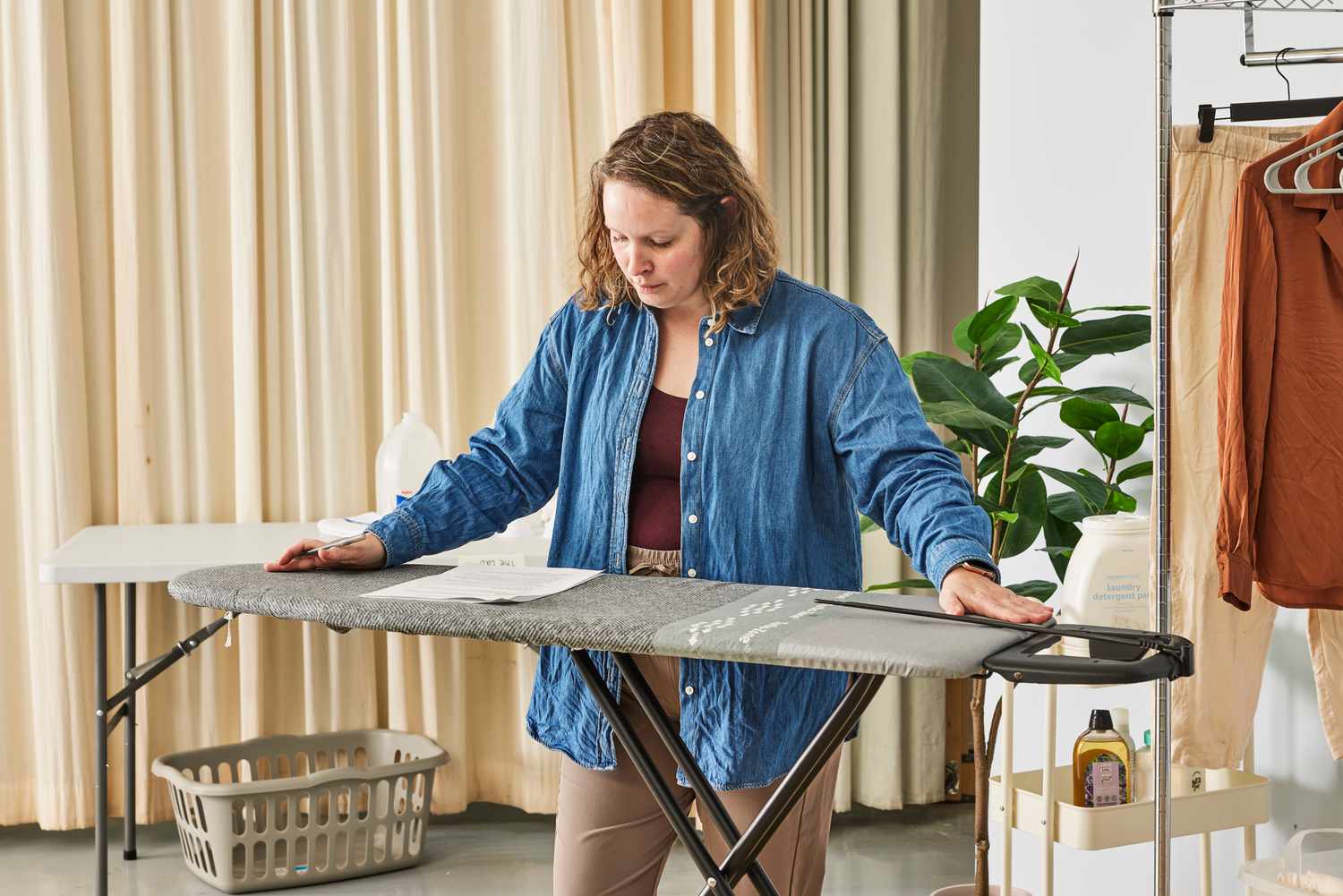 A person pressing down on the Bartnelli Heavy Duty Ironing Board while reading a paper