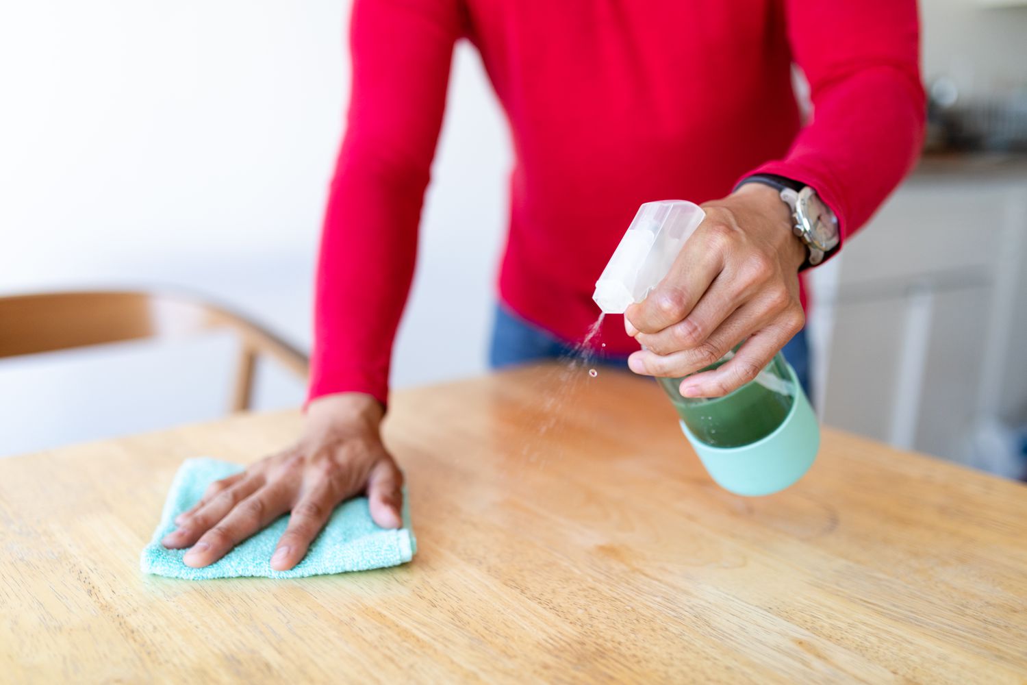 Man cleaning a wooden table with cleaning spray and cloth. 