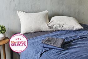 Bed covered with blue linen sheets with two grey pillows next to a grey wall