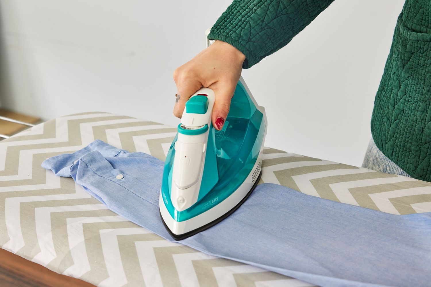 A close-up of a hand pressing an iron into clothes on the Amazon Basics Full-Size Ironing Board 