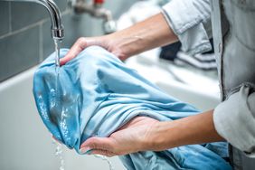 hands holding a stained shirt under running water