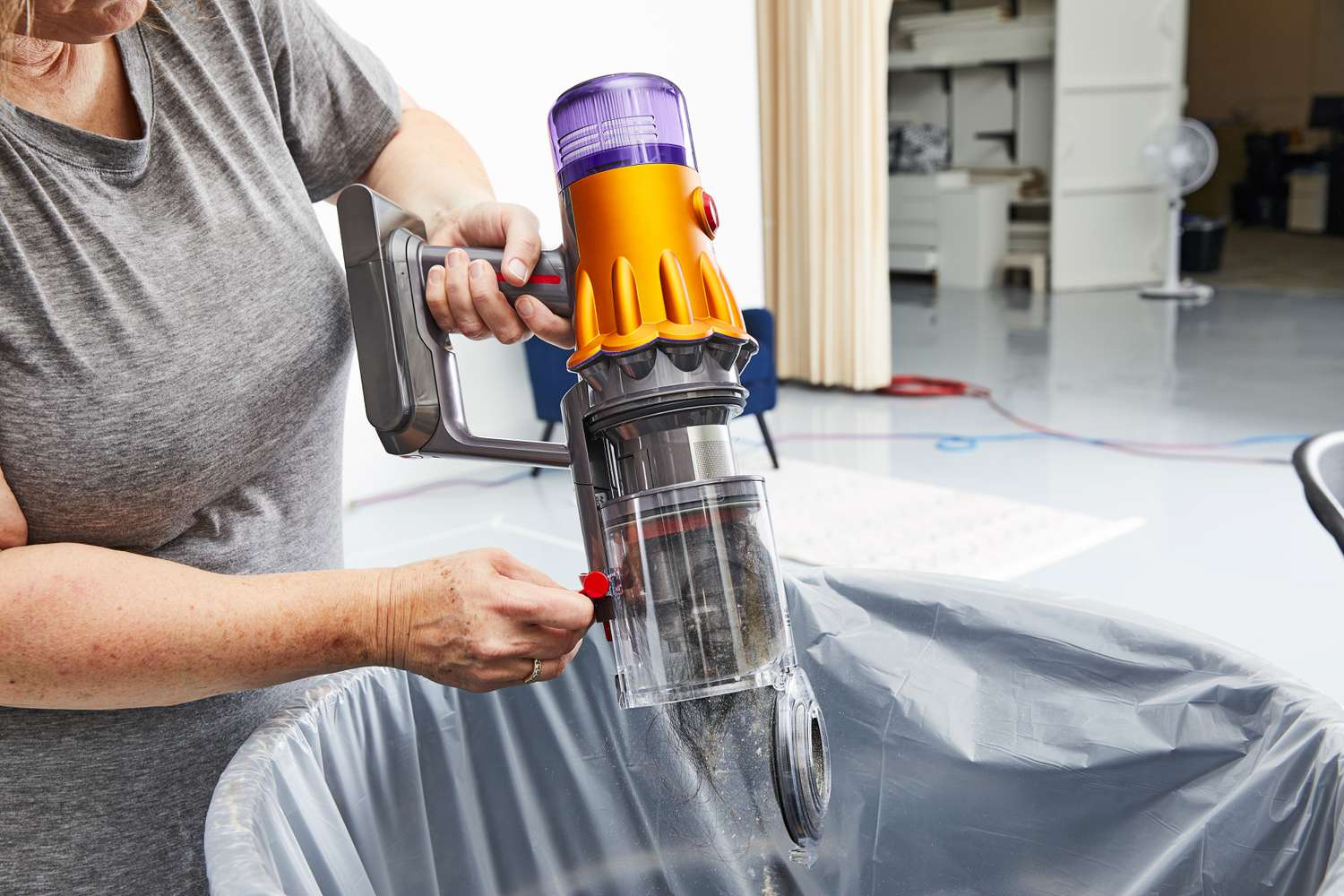 A person emptying dirt and hair from the Dyson V12 Detect Slim into a trash can