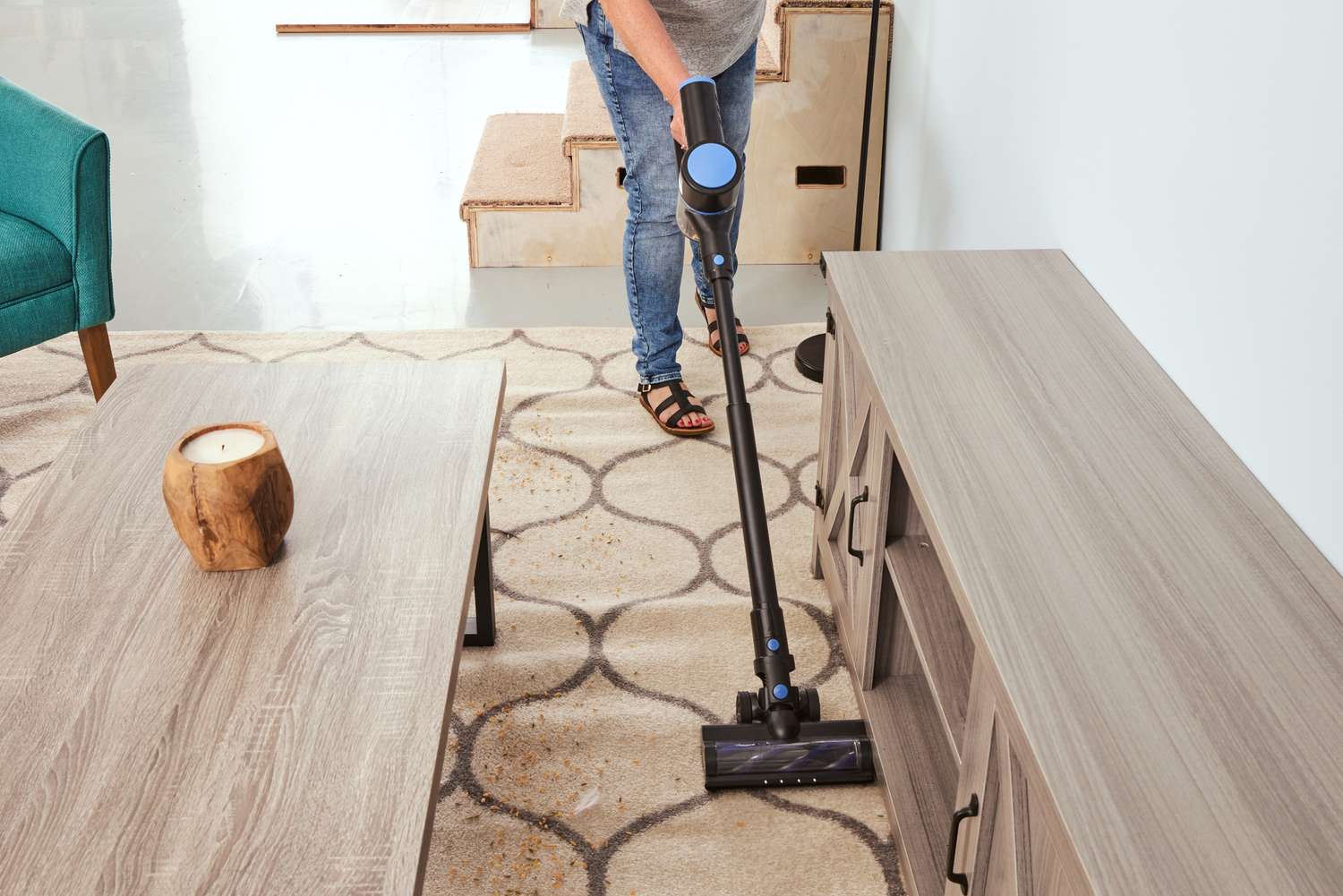 A person uses the WOWGO Cordless Vacuum Cleaner to clean a rug around furniture.
