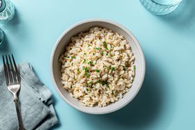 overhead view of a bowl of rice with a napkin, fork and glass on a teal surface