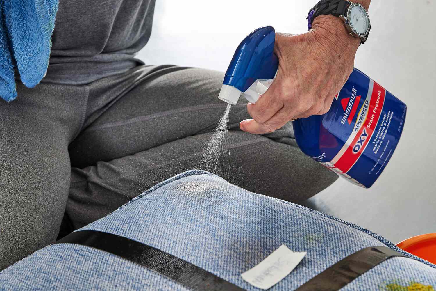 A person spraying Bissell Advanced Oxy Stain Pretreat onto a couch stain.