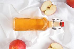 Bottle of Apple Cider Vinegar on White Fabric With Fresh Apples Around It