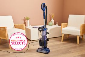 A Shark vacuum standing on wood floor in room with two white chairs